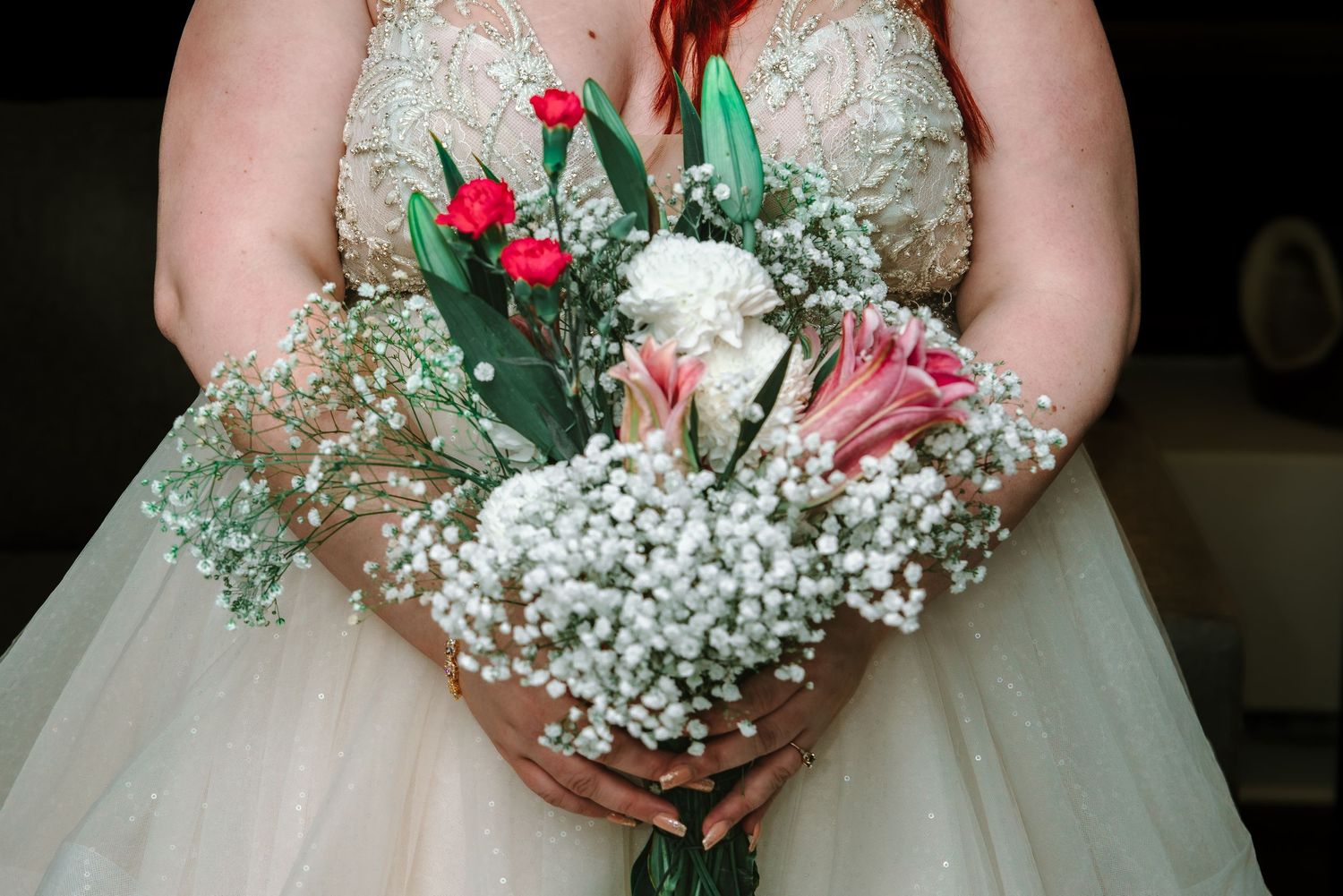 Close-up of bridal bouquet featuring white baby's breath, pink lilies, and red tulips.