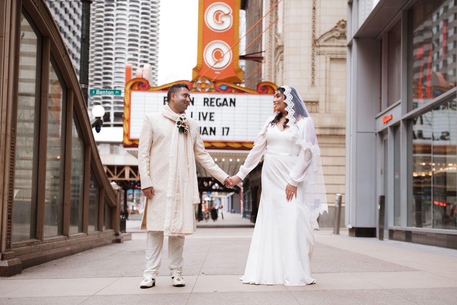 Wedding couple holding hands and smiling outside the historic Chicago Theatre with marquee sign visible.
