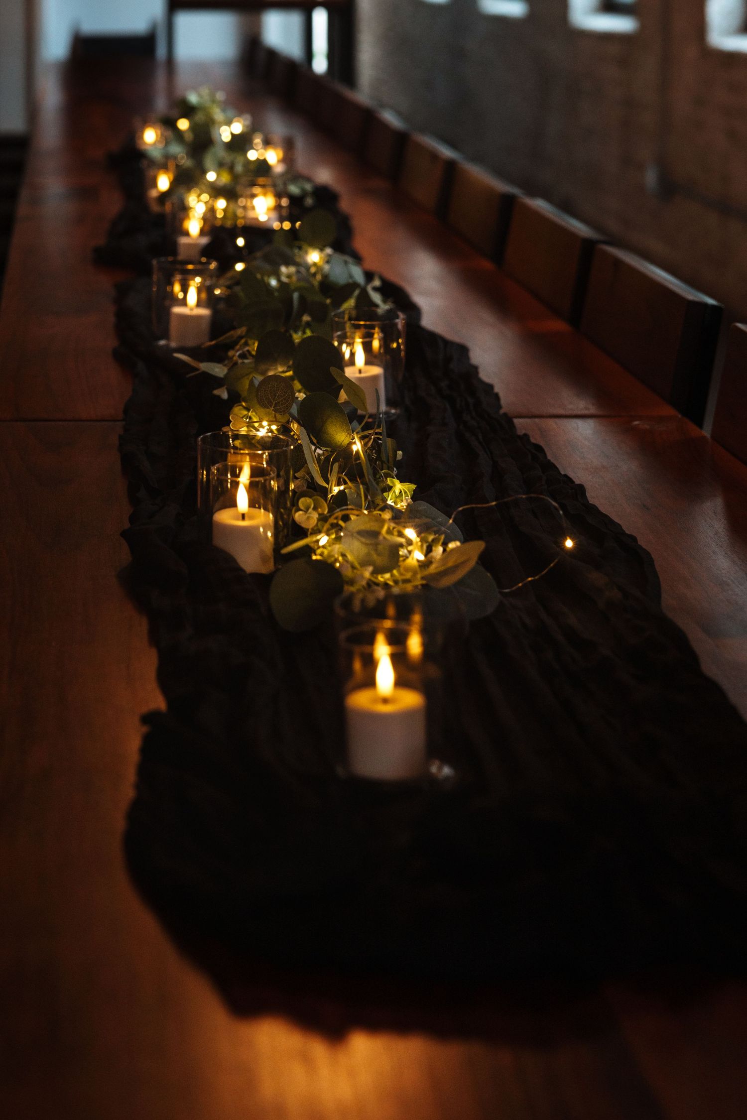 Long wooden reception table decorated with candles and greenery garland centerpiece.