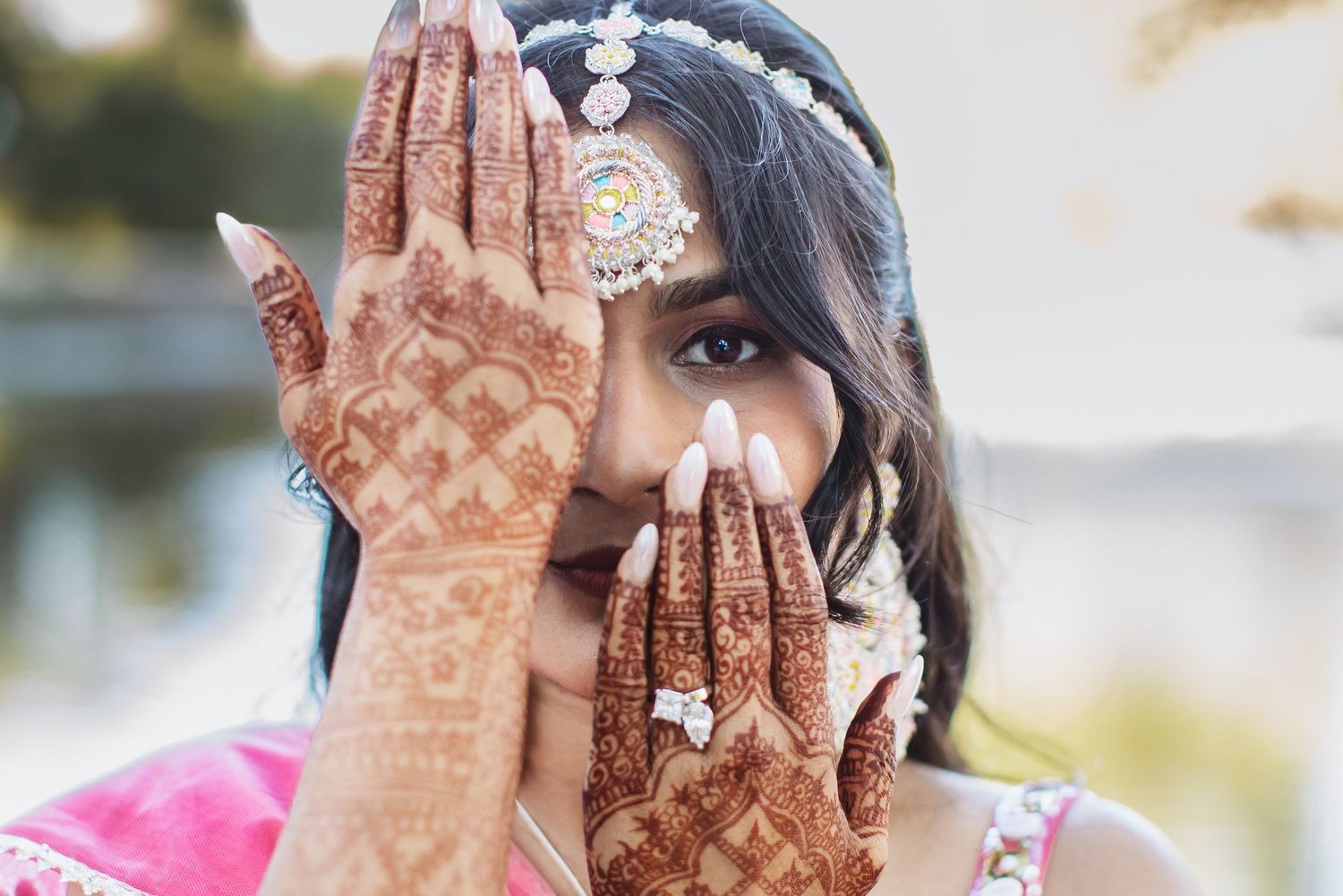 Indian bride in pink lehenga displays intricate mehndi henna designs on both hands.