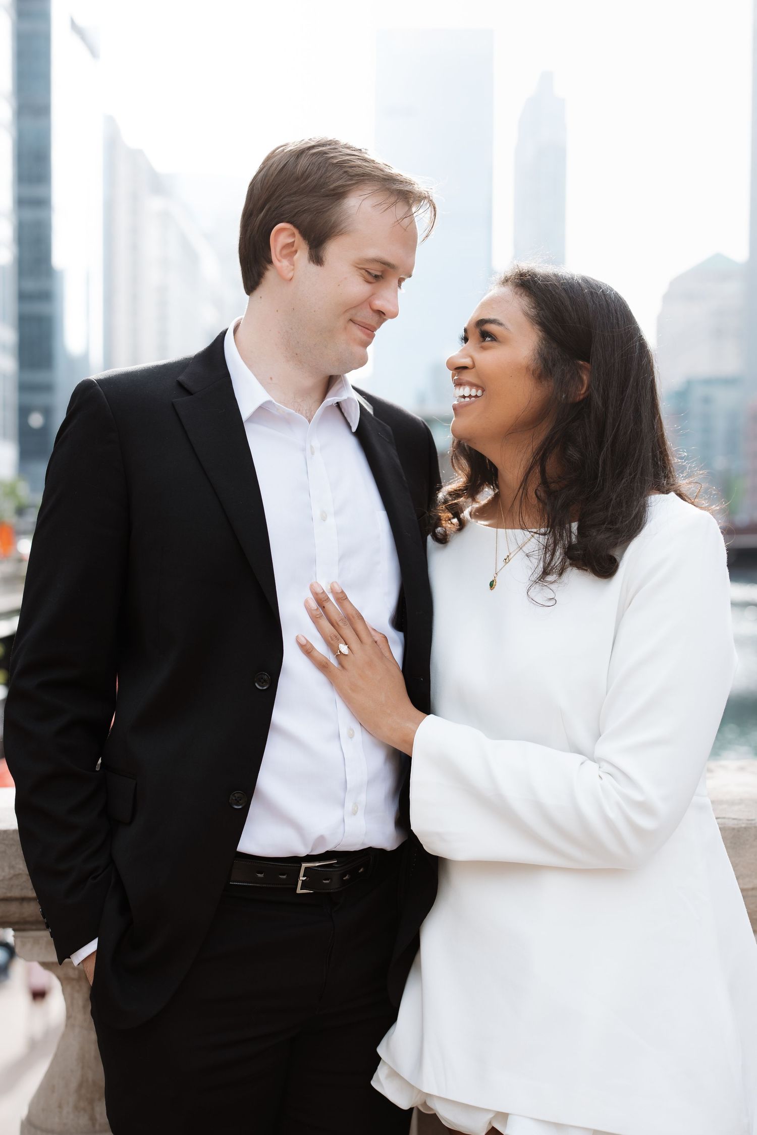 Smiling couple in black and white outfits embracing with city skyline behind them.