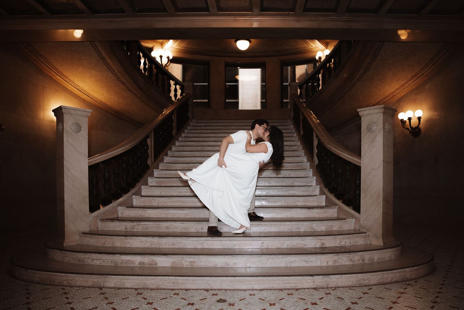 Bride and groom share a romantic dip kiss on the grand marble staircase of a classic Chicago building.