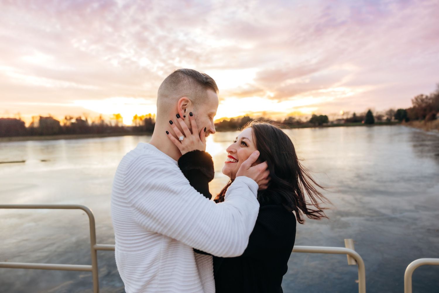 Couple sharing a joyful embrace by the water during a stunning pink and purple sunset.
