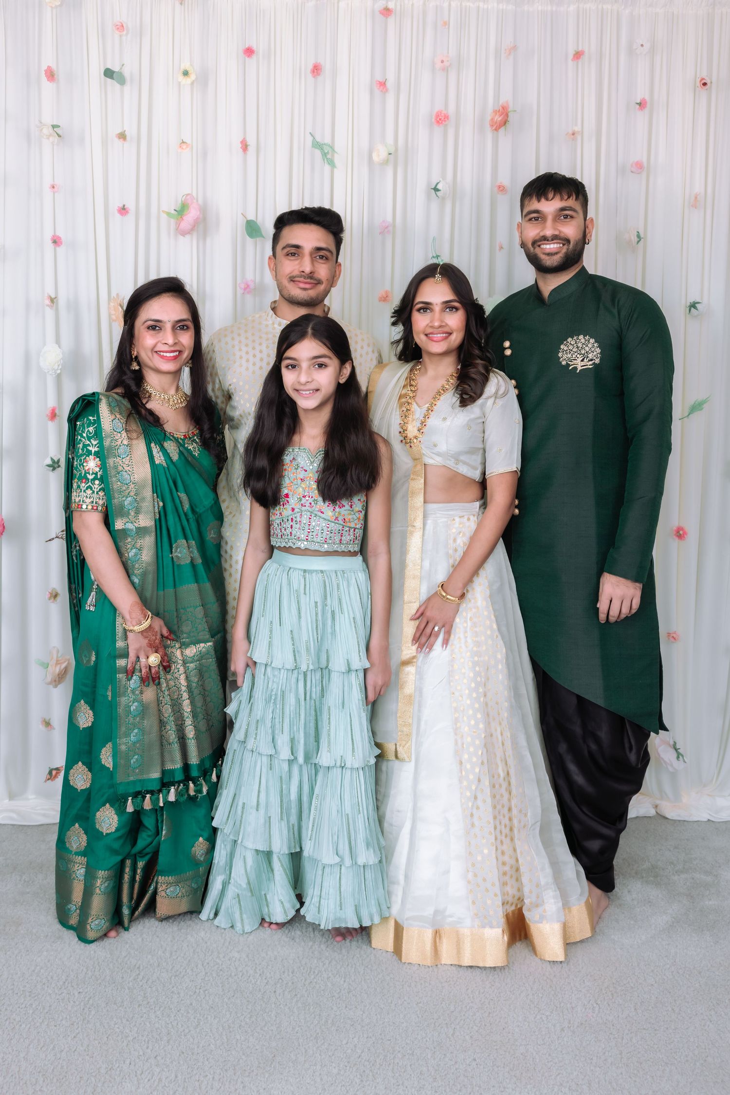 Indian family posing in traditional attire at a festive celebration, wearing green and white outfits with gold accents.