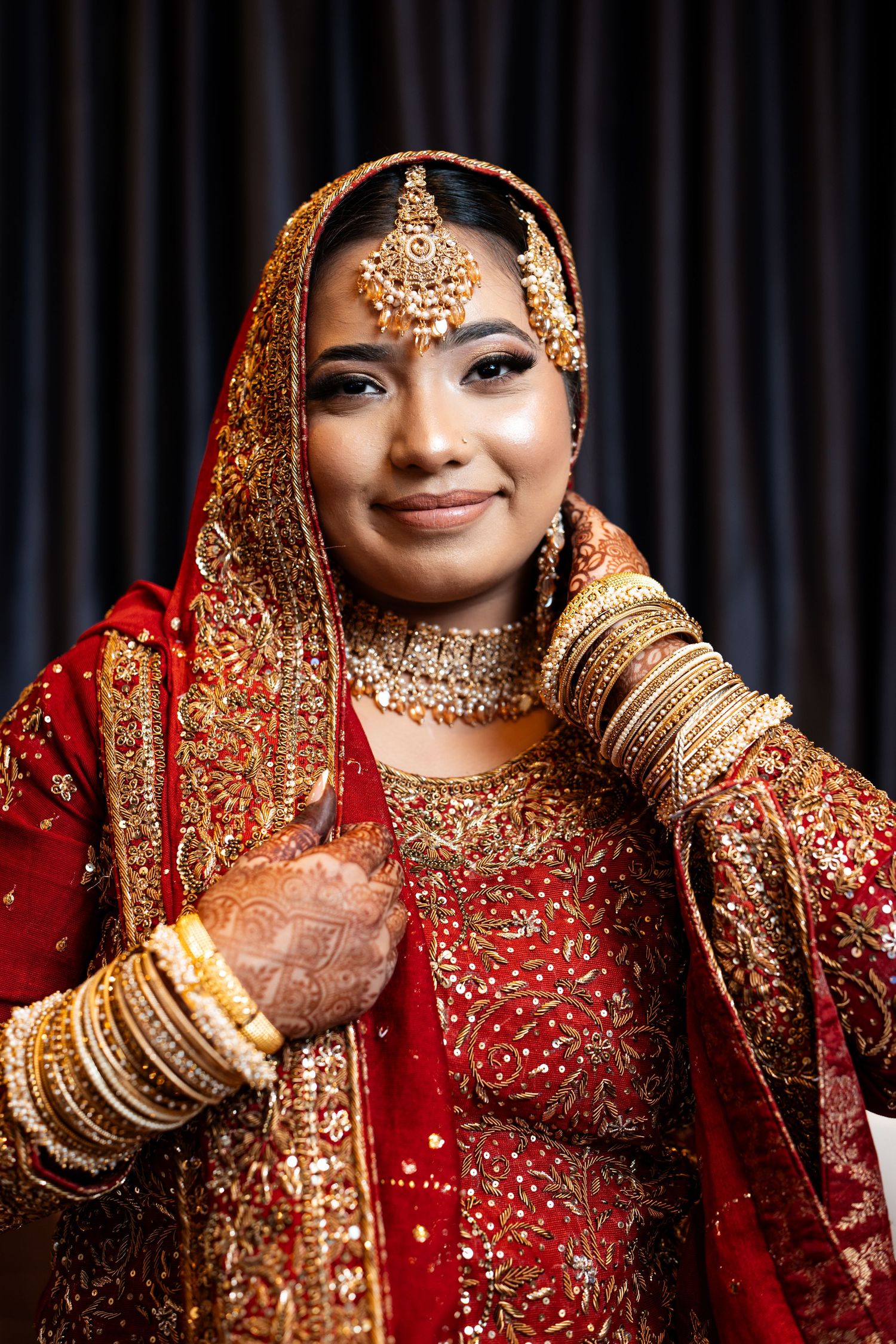 Elegant Indian bride smiling in red and gold lehenga with traditional gold bridal jewelry.