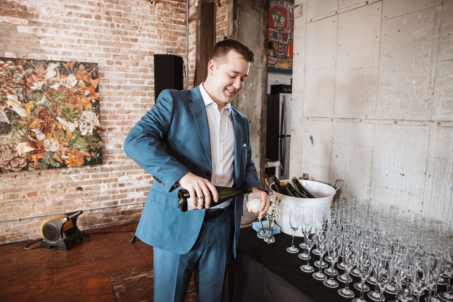Man in blue suit smiles while pouring champagne into glasses at an elegant event.