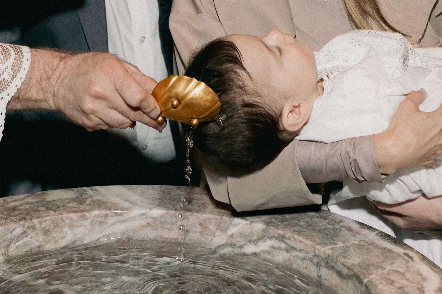 Close-up of a priest pouring holy water over an infant's head at a baptismal font during christening.