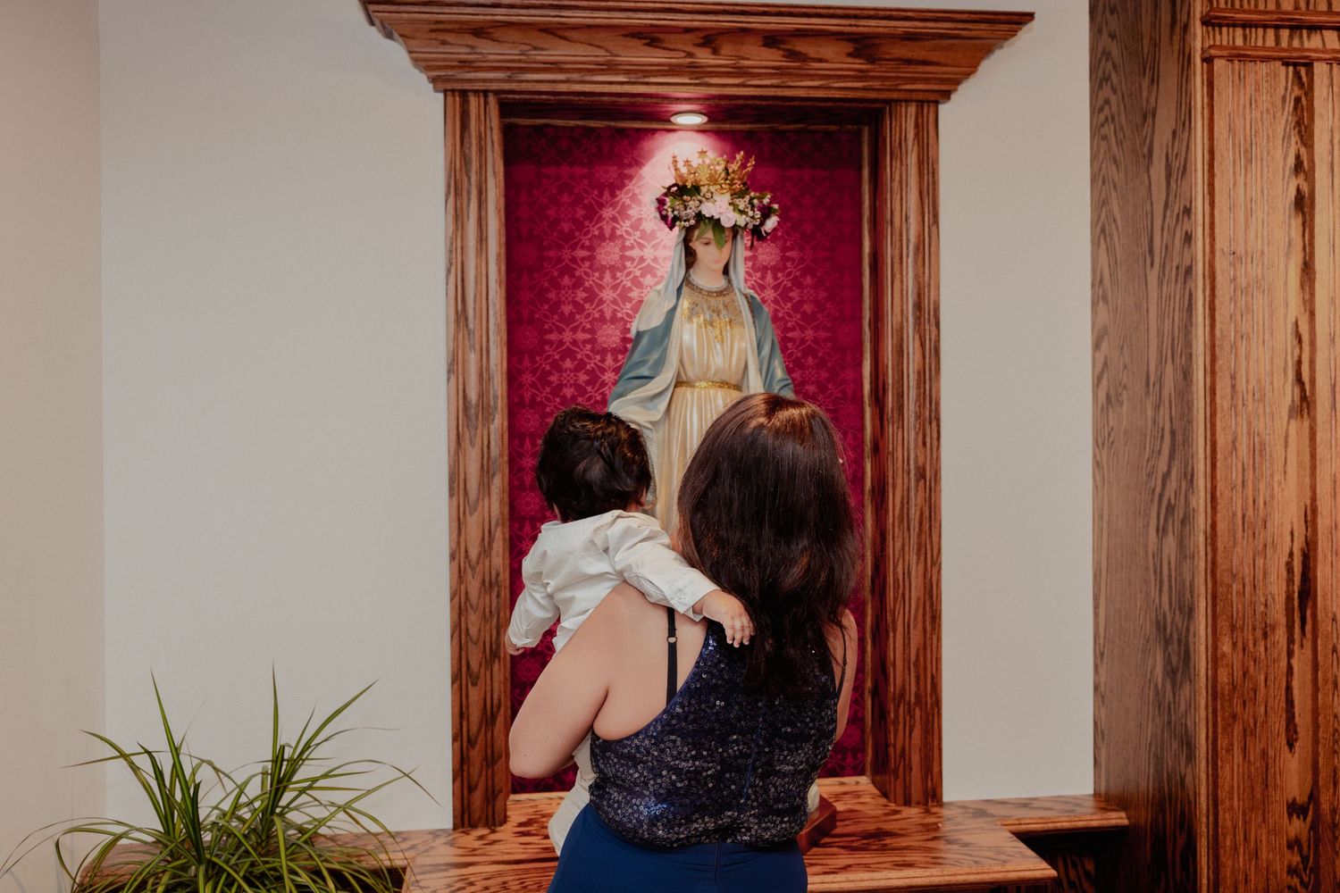 Mother holds baby while praying before Virgin Mary statue in Catholic church.