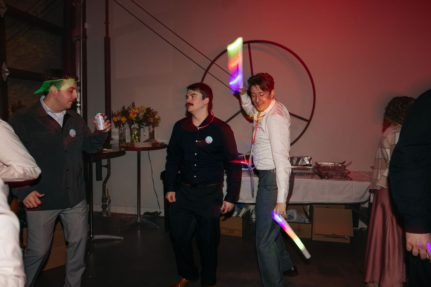 Wedding guests dancing and celebrating with colorful glow sticks at a festive reception party.
