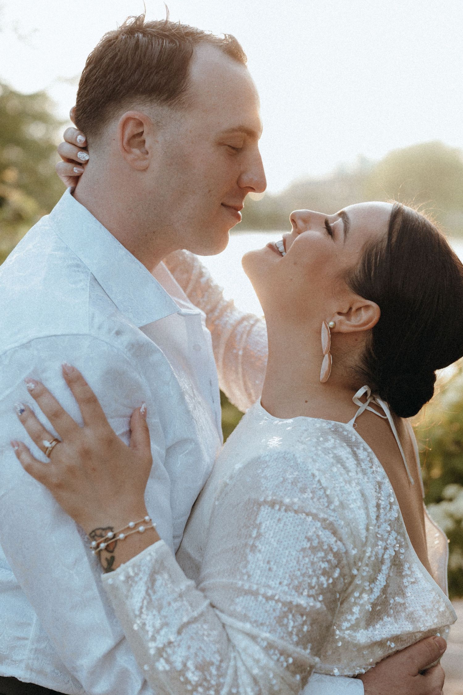 A couple shares a romantic moment, the woman laughing joyfully as they embrace outdoors in soft golden light.