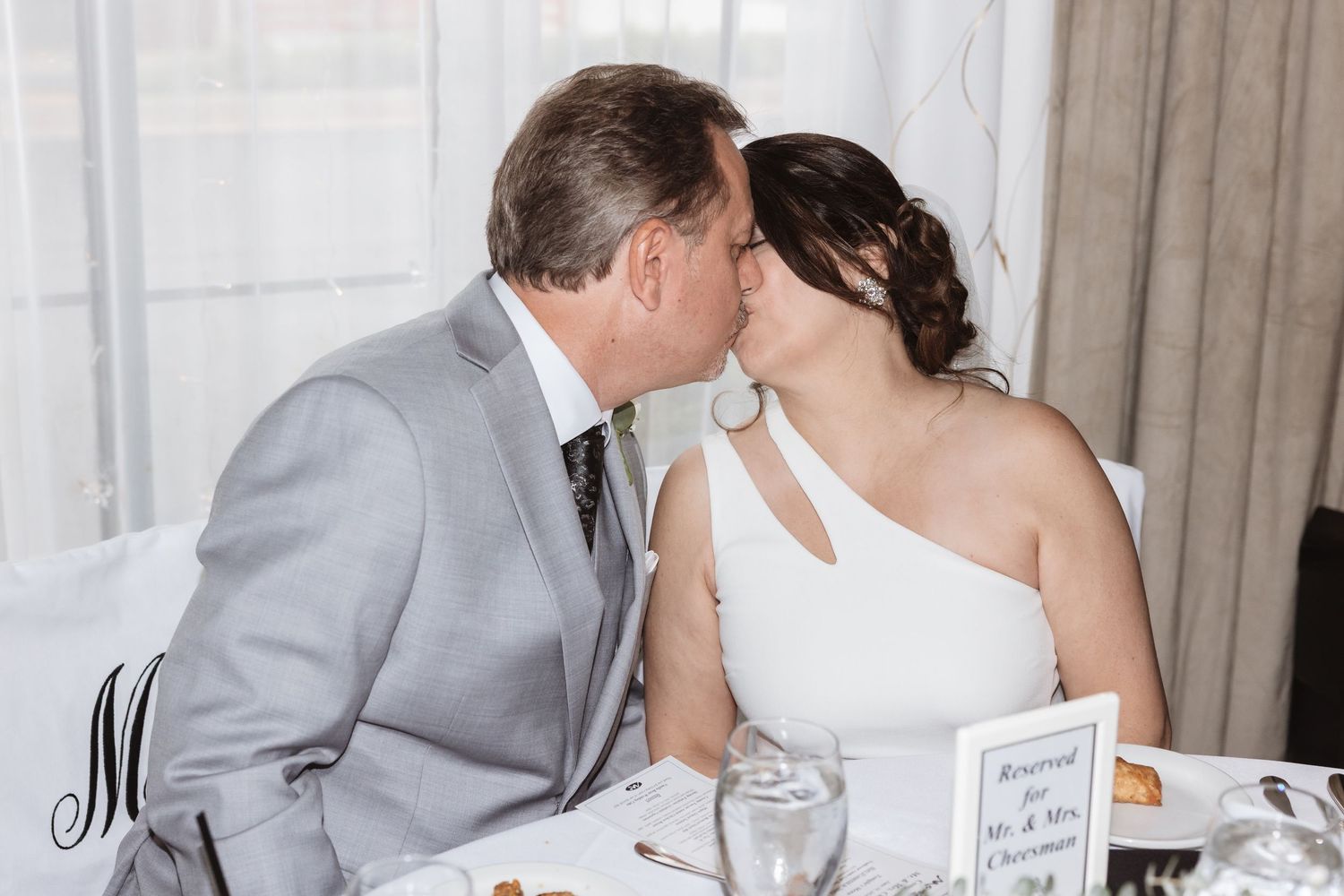 Bride and groom sharing a kiss while seated at the head table during their wedding reception.