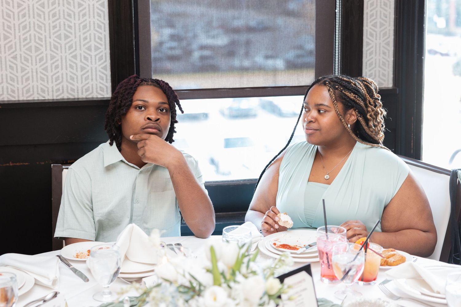 Two young women seated at a wedding reception dinner table with floral centerpieces.