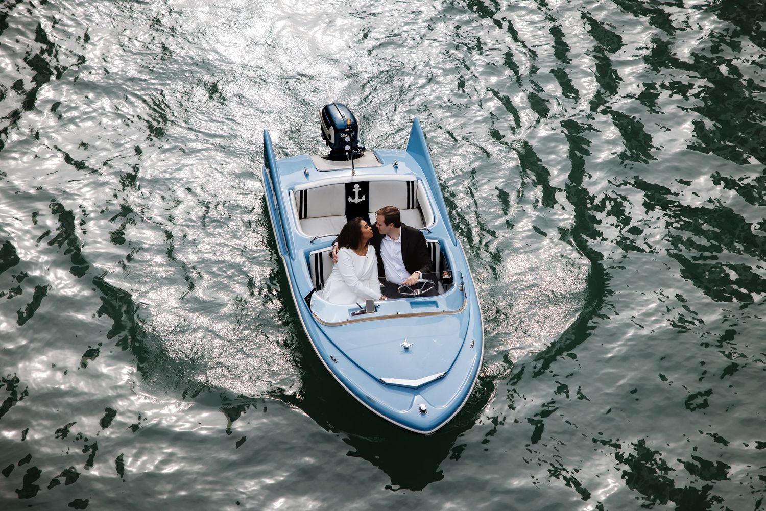Aerial view of a couple kissing on a small blue boat surrounded by sparkling water in Chicago.