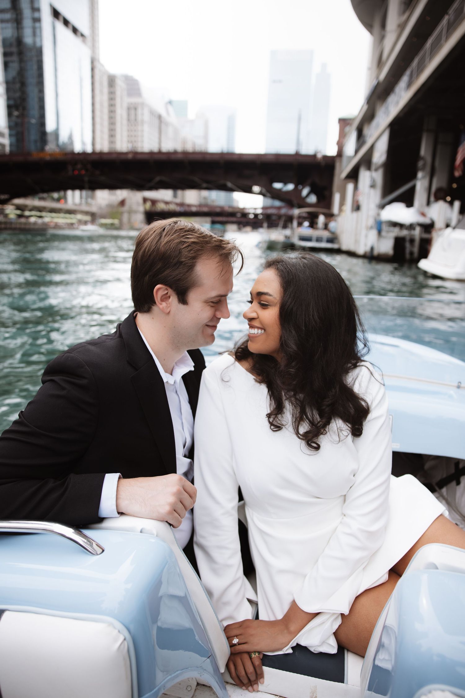Couple sharing a romantic moment on a vintage blue boat along the Chicago River with city bridges in the background.