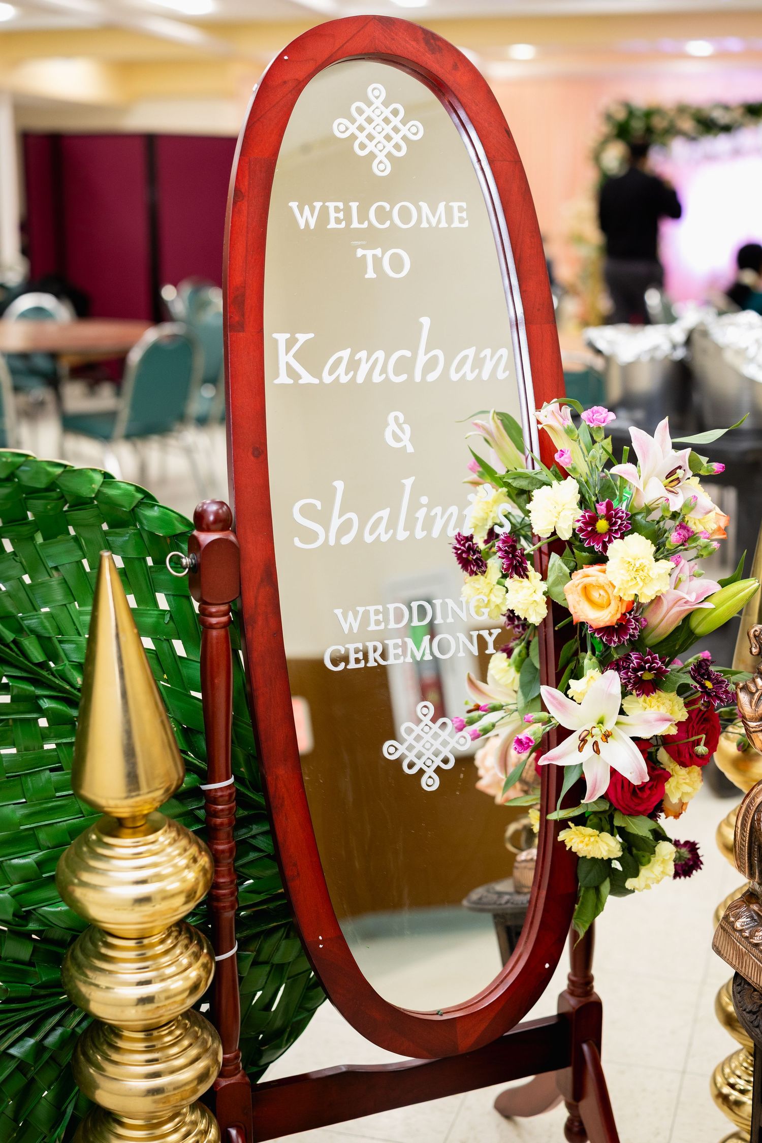 Welcome mirror sign for Kanchan and Shalini wedding ceremony decorated with colorful fresh flowers at Indian wedding venue.