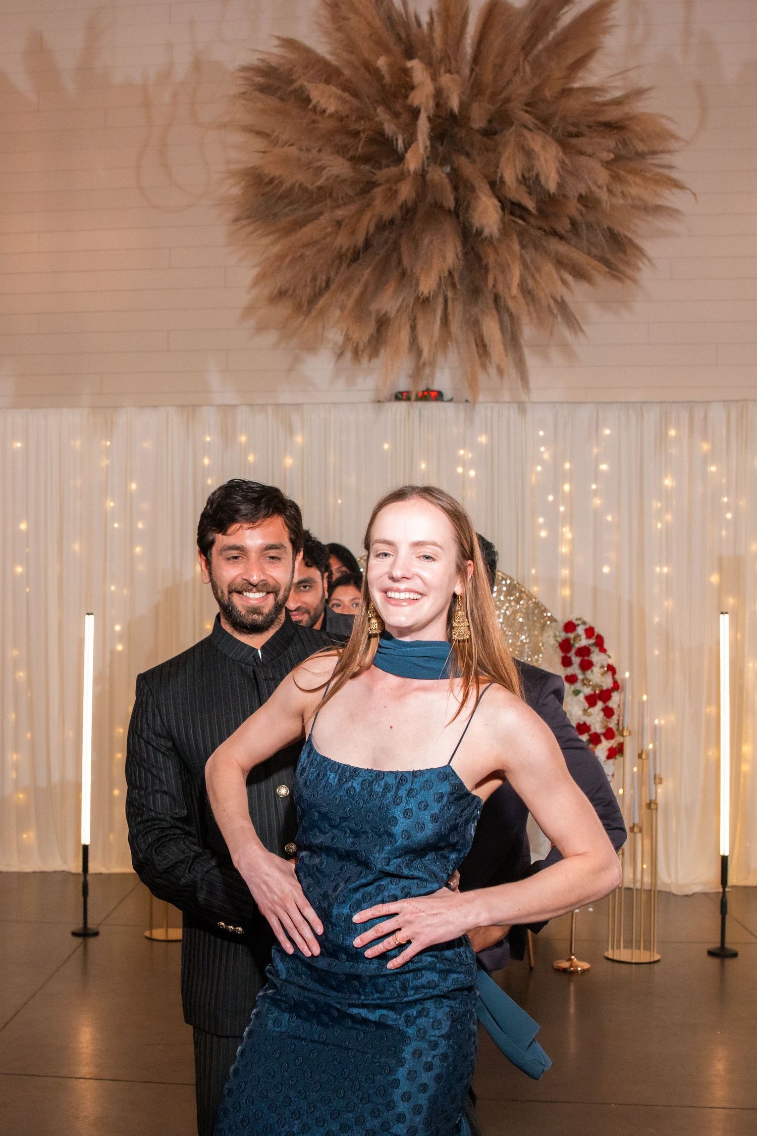 Smiling couple dancing at elegant wedding reception with fairy light backdrop.
