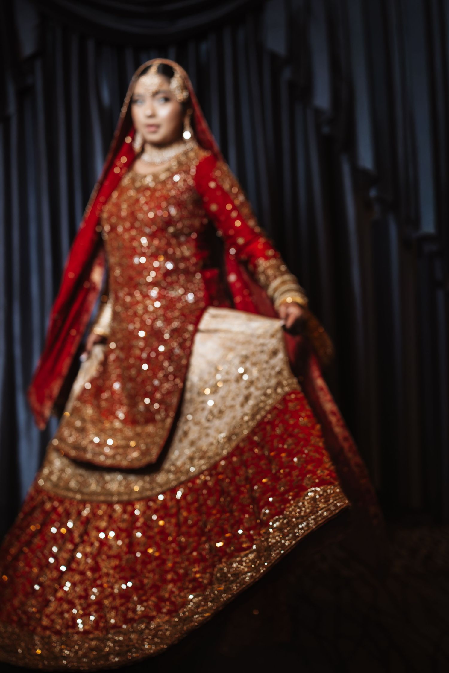 South Asian bride twirling in stunning red and gold sequined lehenga bridal outfit with dupatta.