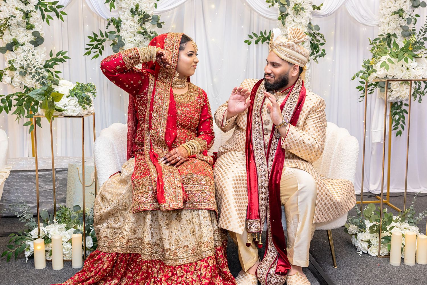 South Asian bride and groom in red and gold traditional attire seated at wedding ceremony.
