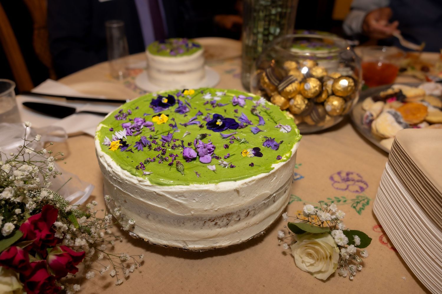 Decorated wedding cake with green frosting and purple flowers on a festive reception table.