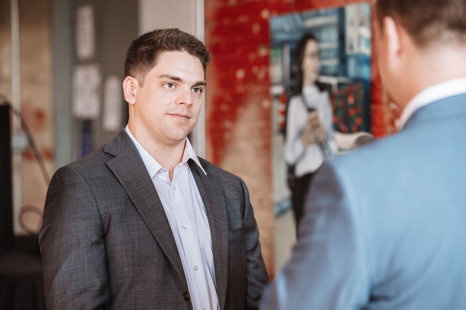 Man in gray suit jacket having a conversation at a formal indoor event with guests.