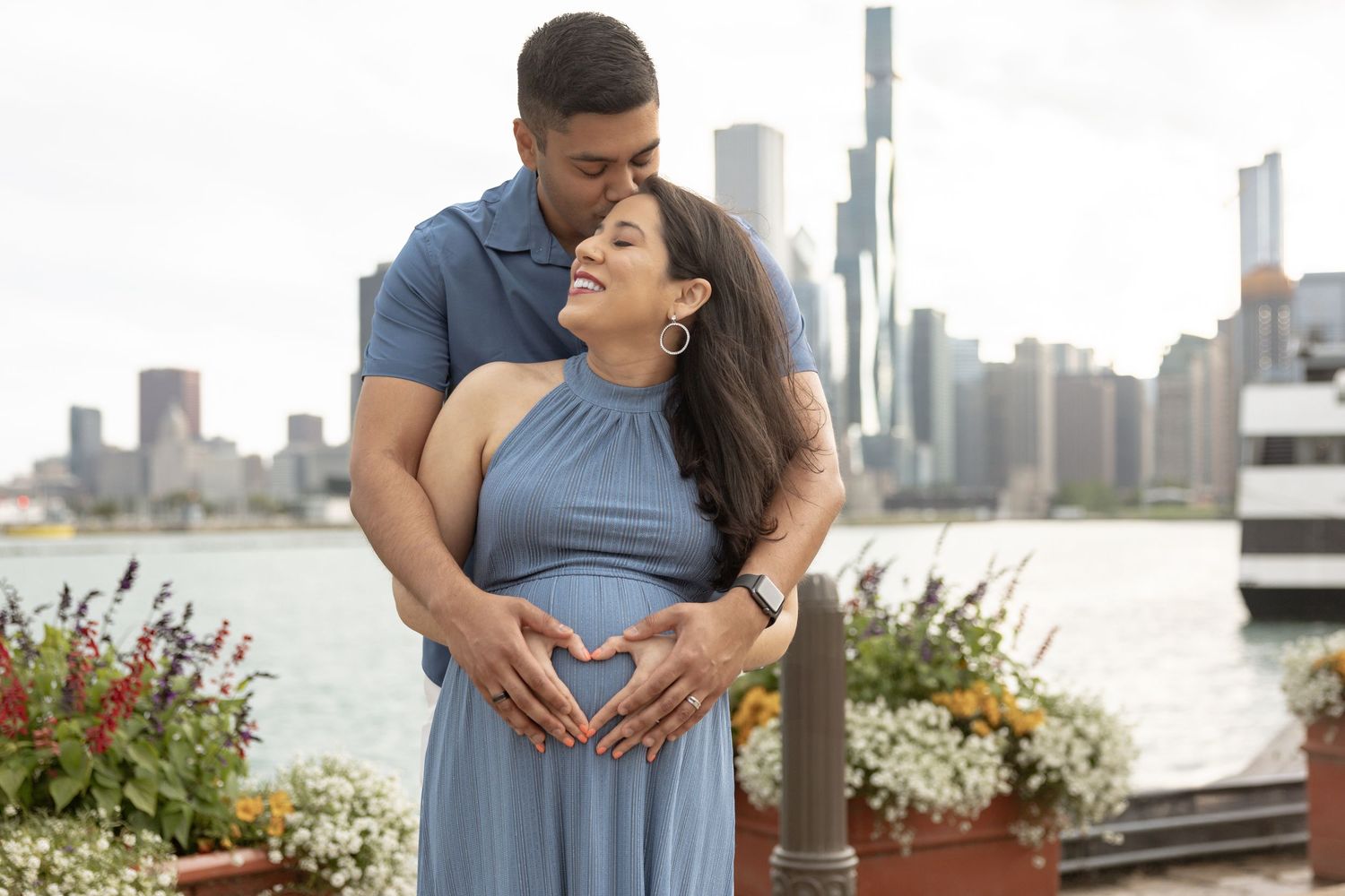 Couple forming heart shape with hands over pregnant belly with Chicago city skyline in background.