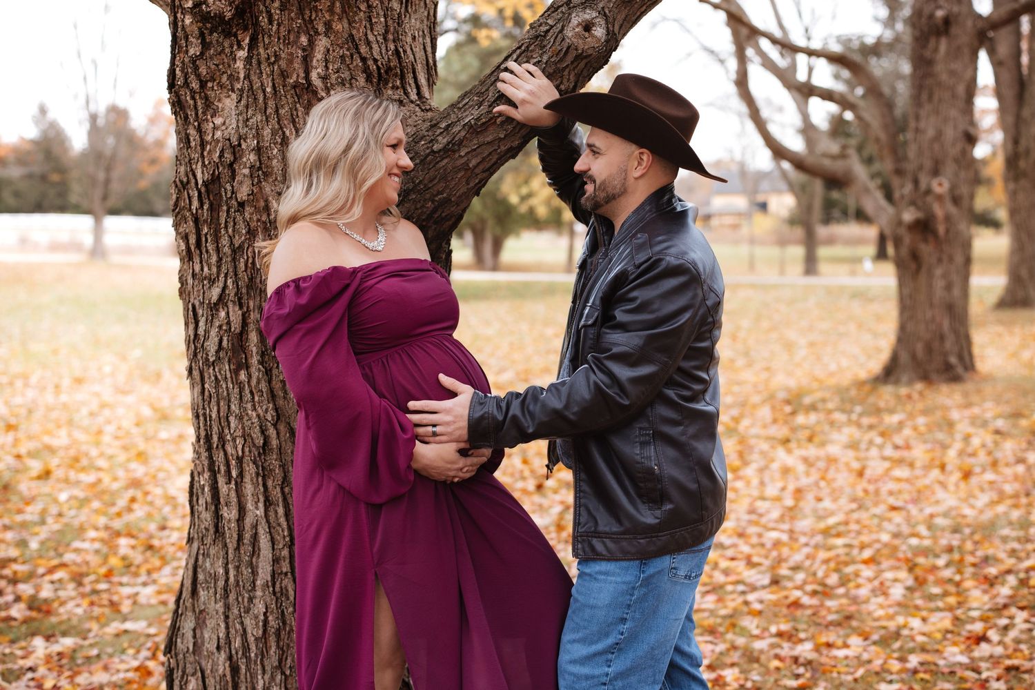 Expecting couple in fall park, man in cowboy hat tenderly holds pregnant womans belly.