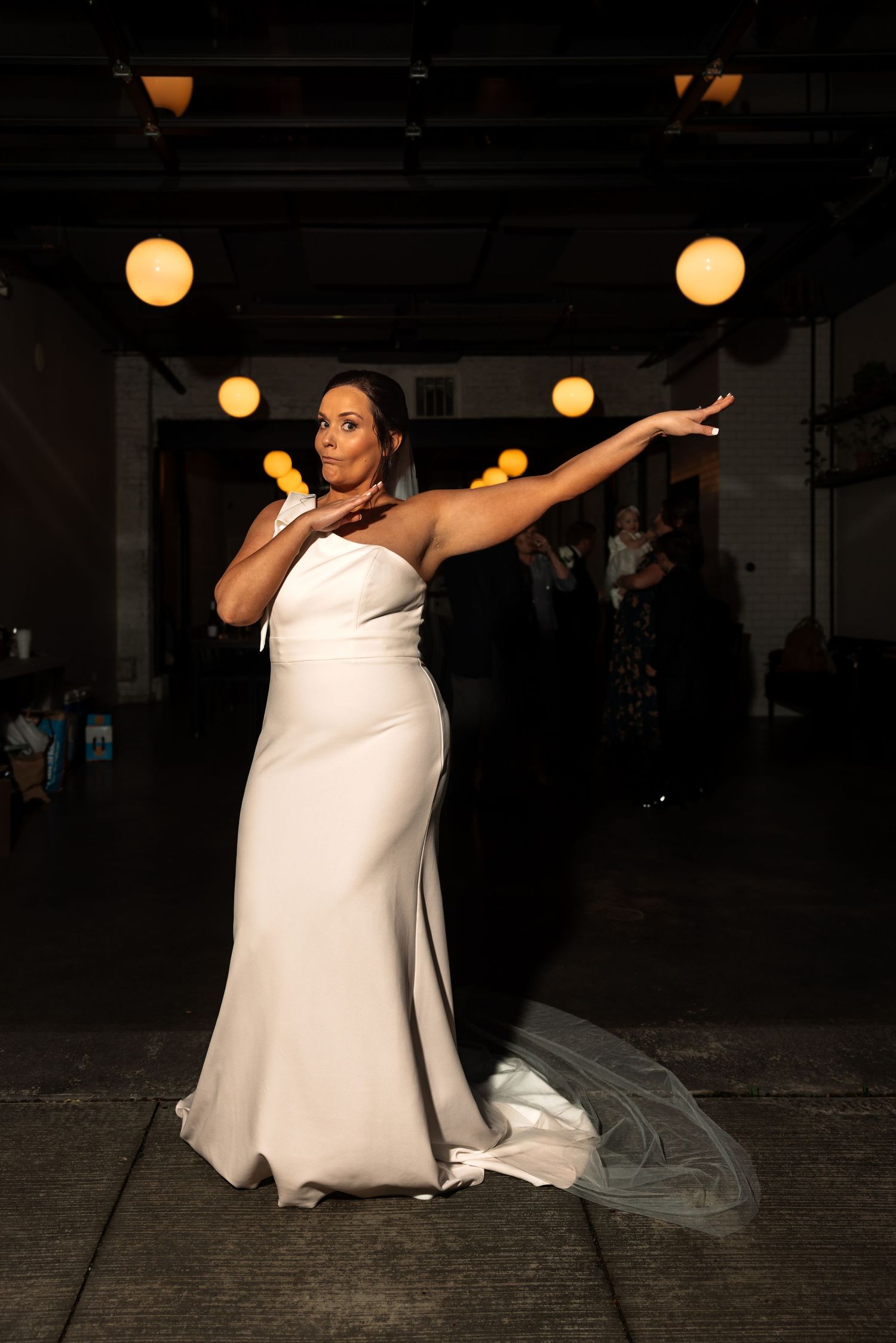 Bride in a white one-shoulder gown striking a dramatic pose at her reception.