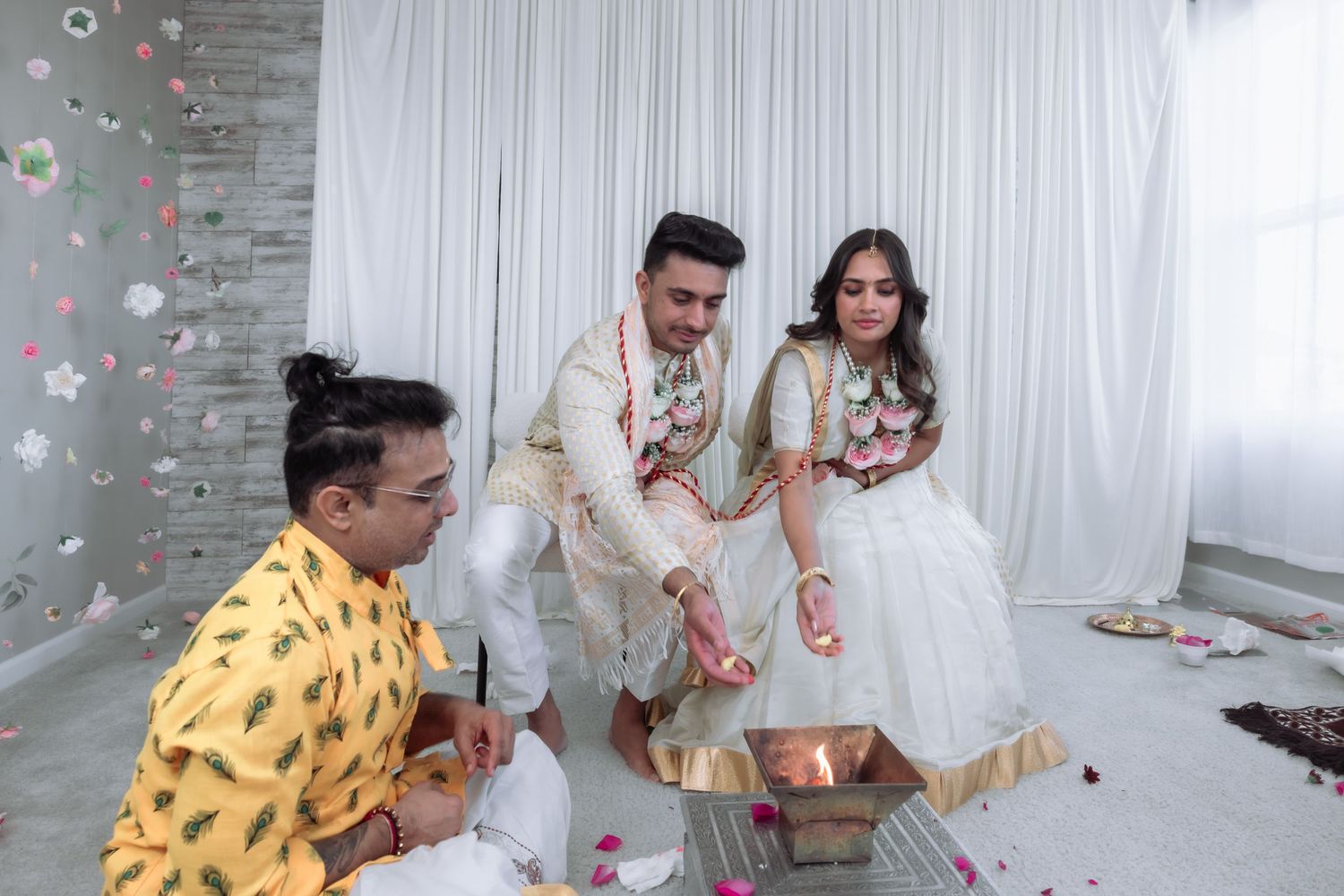 Couple performing Hindu wedding fire ritual with priest in white studio.