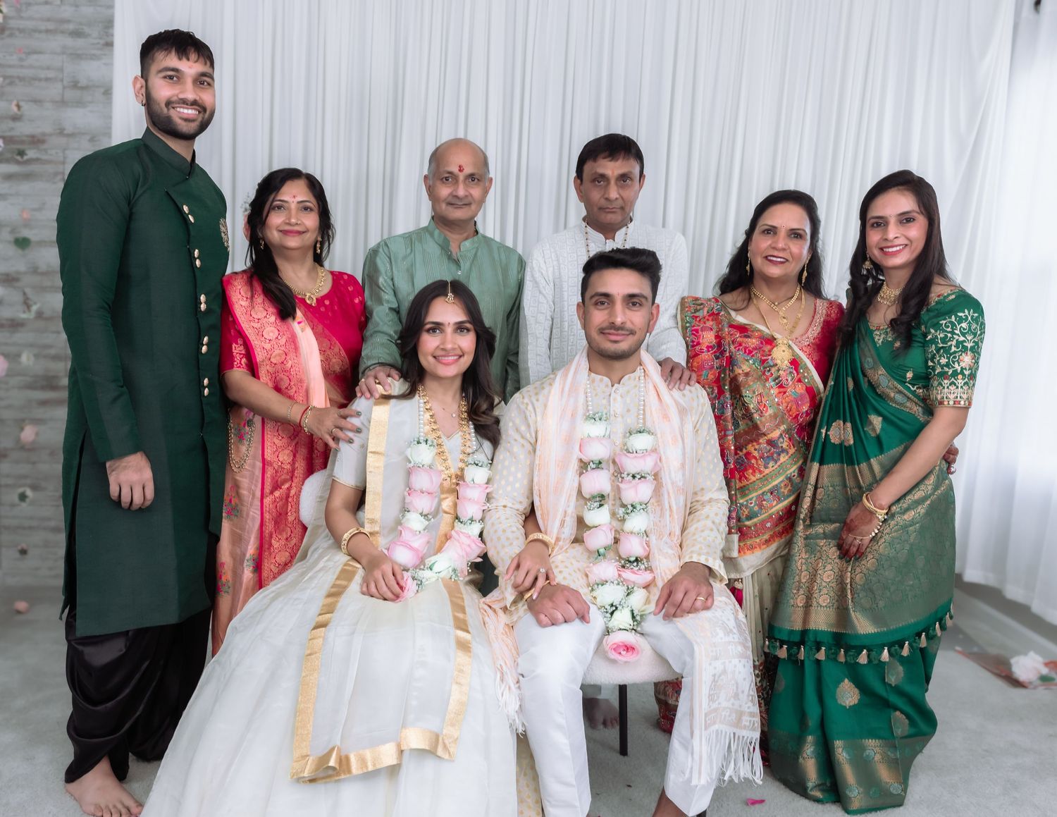 Extended family portrait at Indian engagement with seated couple in ceremonial garlands.