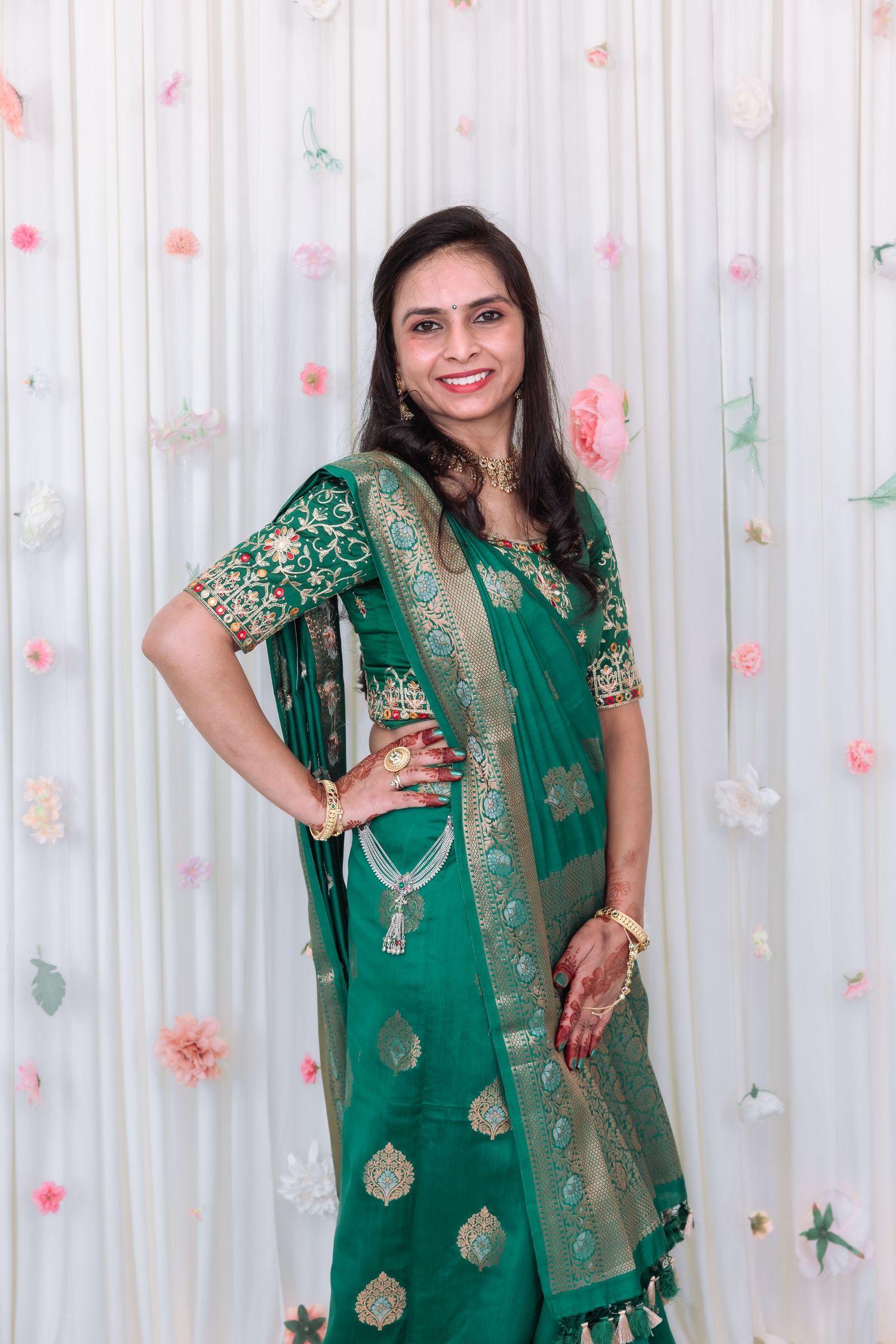 Smiling Indian woman in elegant green gold Banarasi saree poses at decorated wedding celebration.