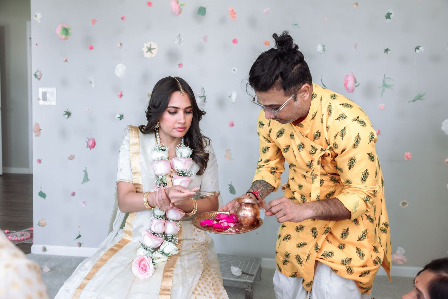 Groom in yellow kurta performs traditional ritual with bride in white lehenga during Indian wedding ceremony.
