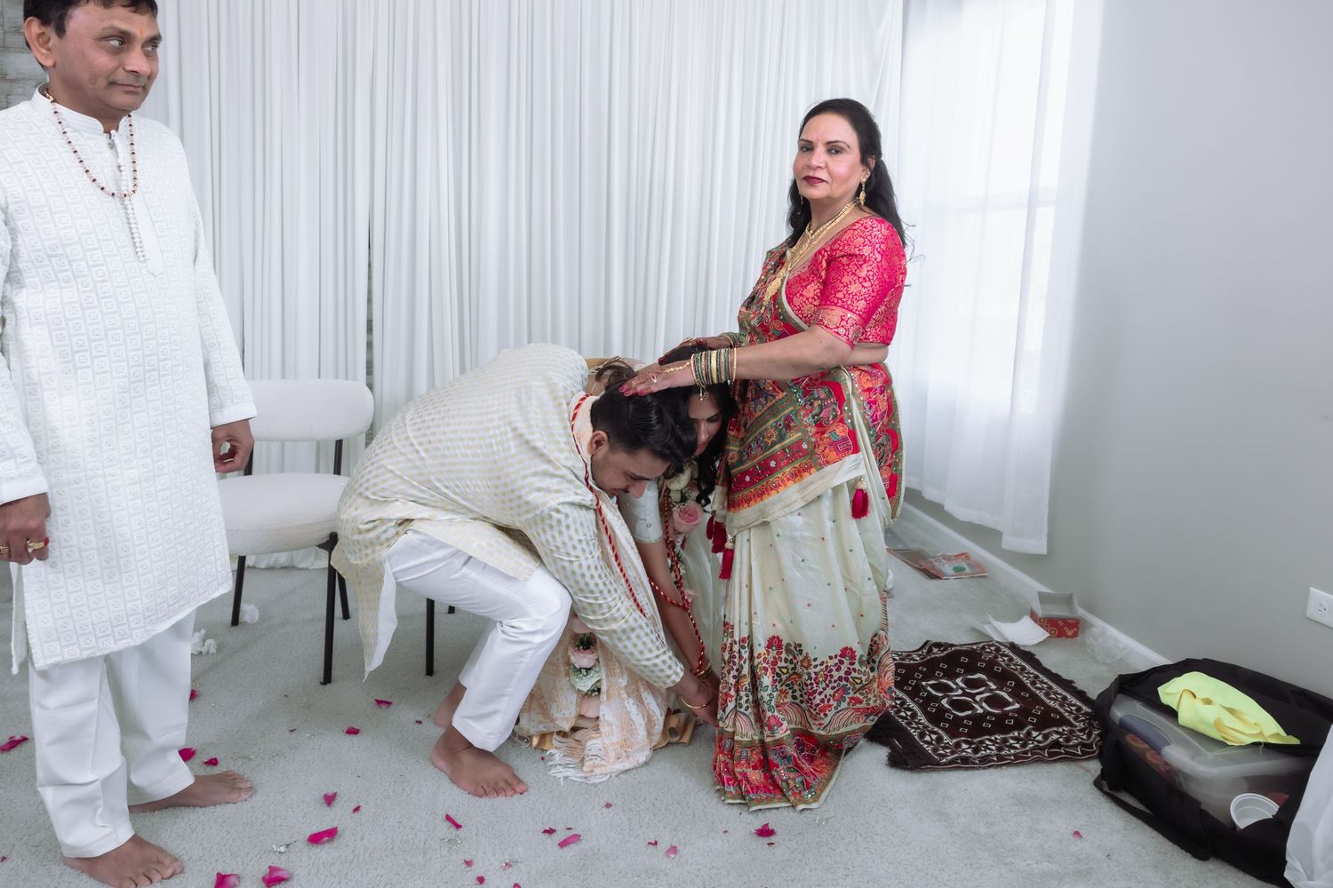 Indian wedding ceremony with groom performing traditional foot-touching ritual with smiling family.
