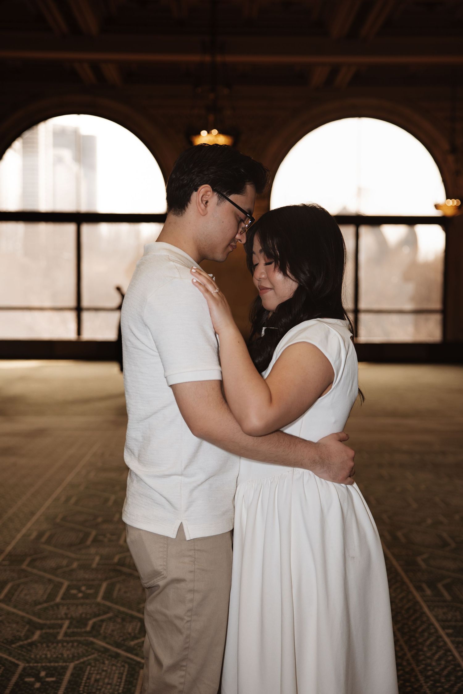 Couple leans in close together in a tender embrace inside the golden-lit hall of the Chicago Cultural Center.