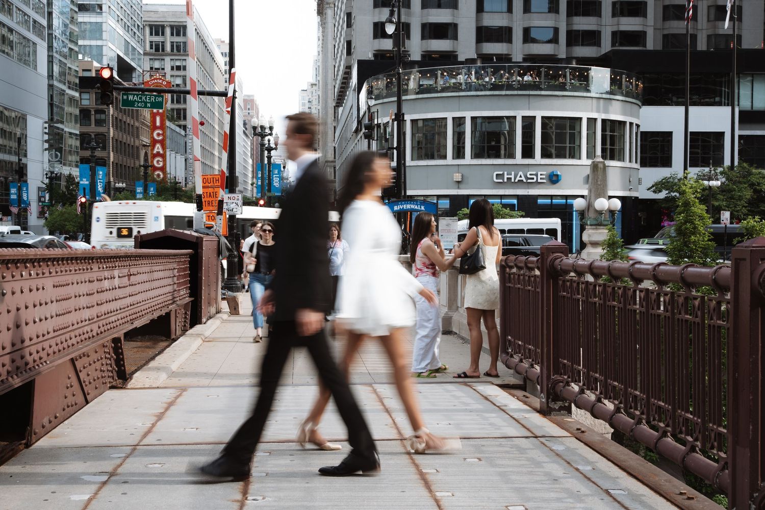 Motion blur photo of couple walking across a Chicago bridge with a Chase bank tram passing by.