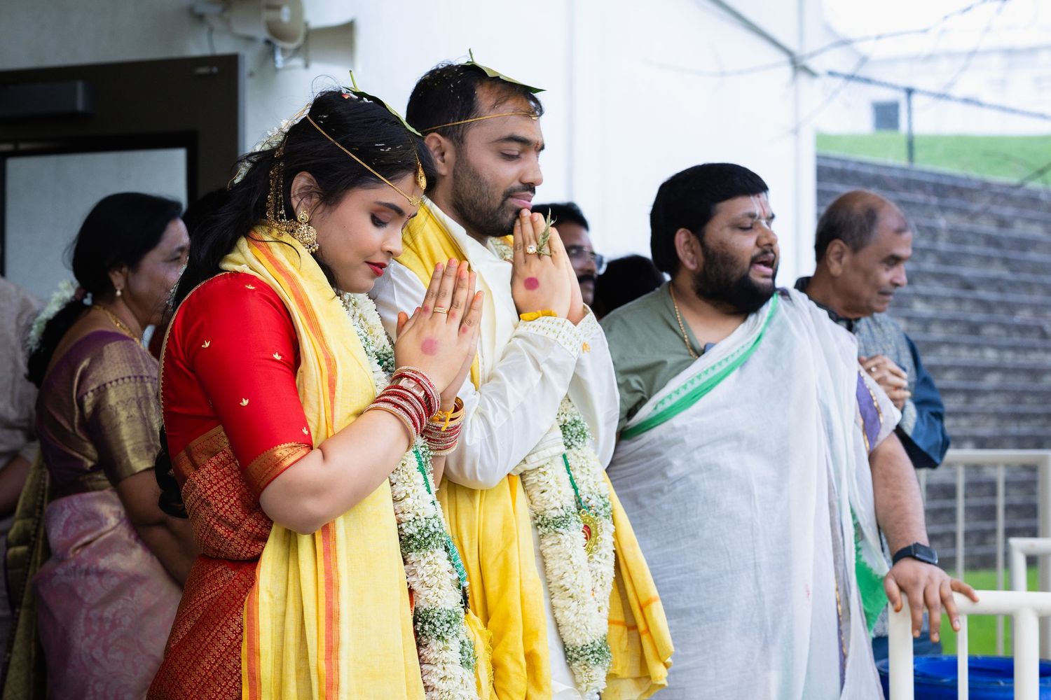 Indian bride and groom in yellow ceremonial scarves performing prayer gesture at traditional Hindu wedding.