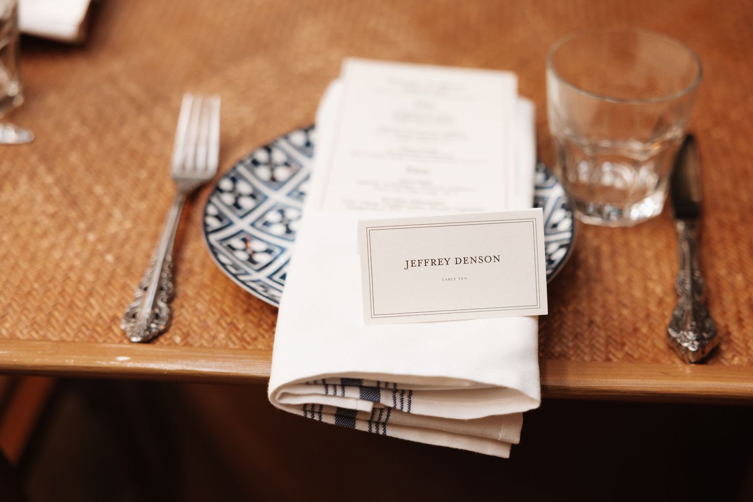 Elegant wedding place setting with monogrammed name card, patterned plate, silverware, and folded linen napkin.