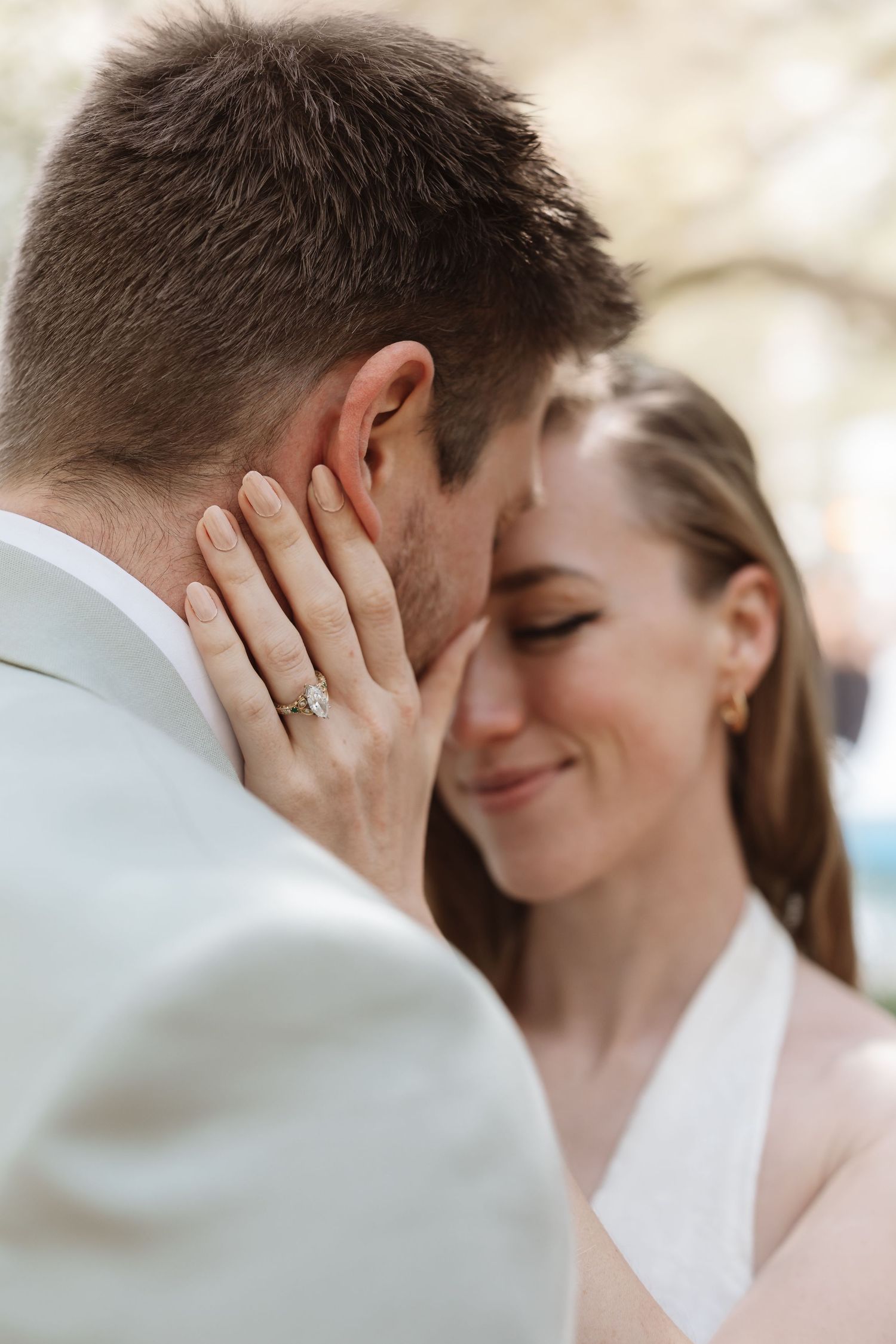Close-up of bride smiling with diamond ring visible as she cradles grooms face.