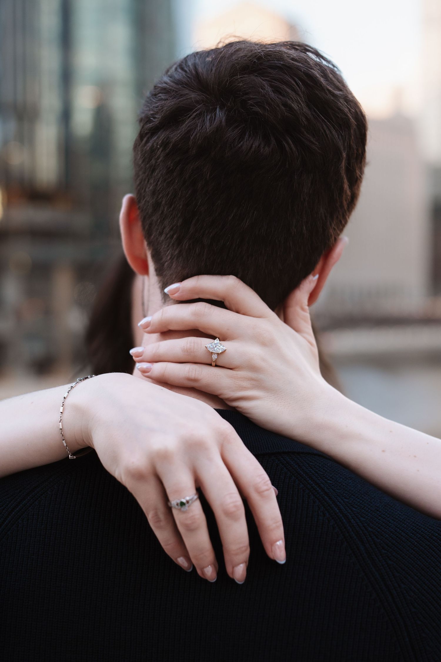 Close-up of an engaged womans hand with diamond ring resting on her partners neck.