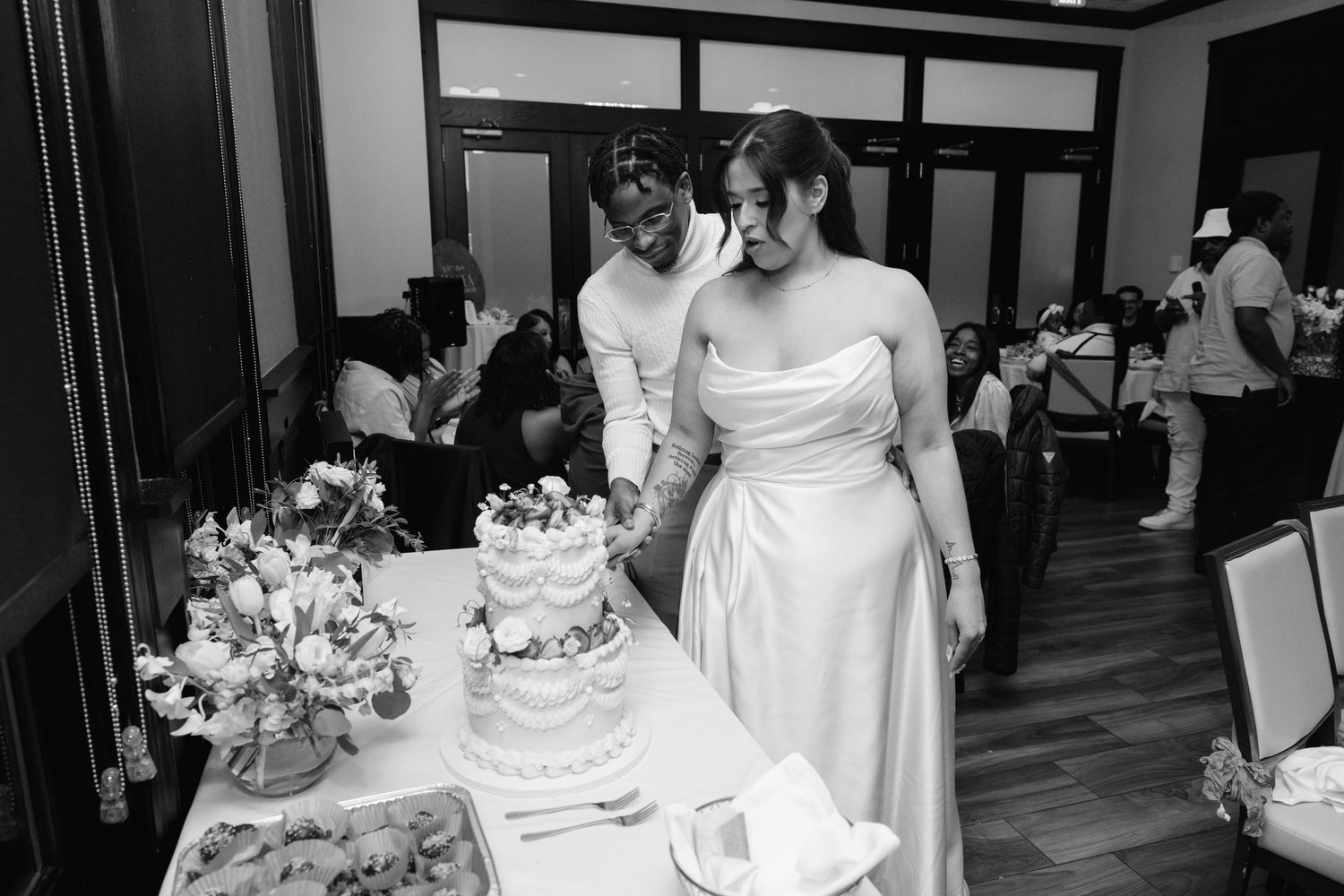 Bride and groom cutting their wedding cake together in black and white photo.