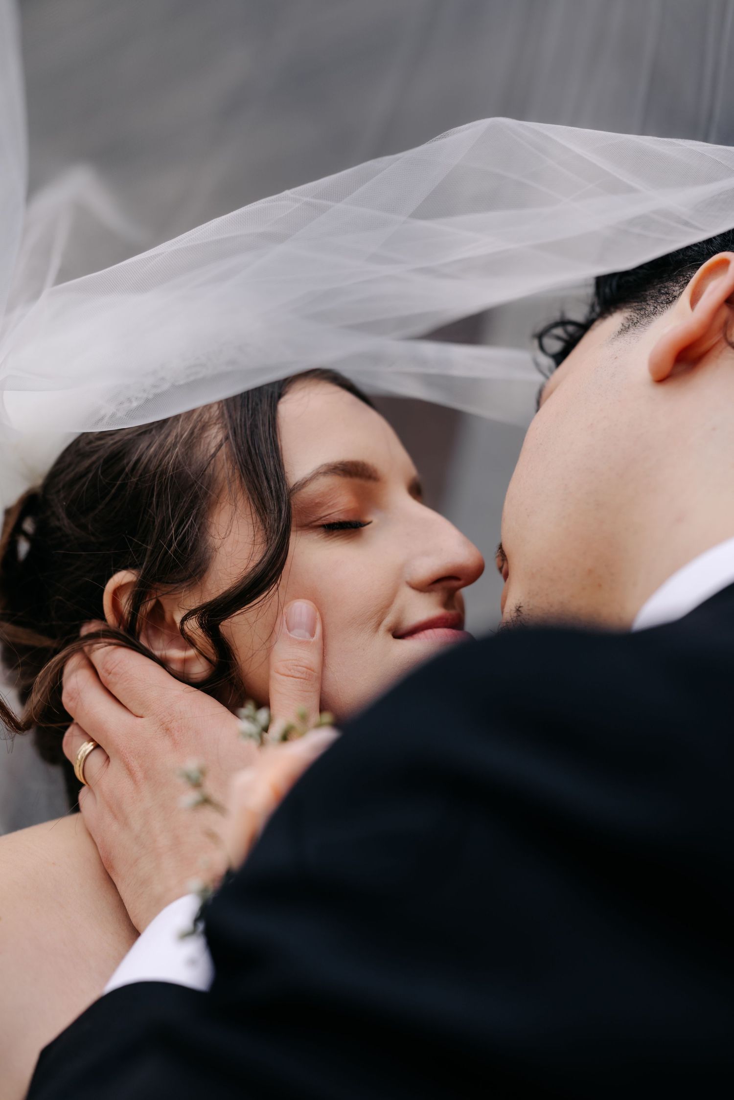 Bride and groom sharing a romantic moment under a white veil, with the groom tenderly cupping the bride's face.