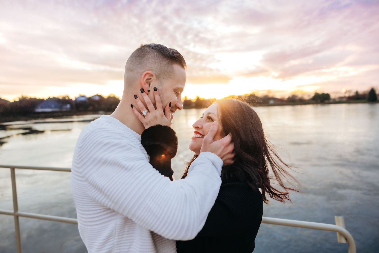 Couple embracing tenderly at golden hour sunset by a shimmering waterfront.