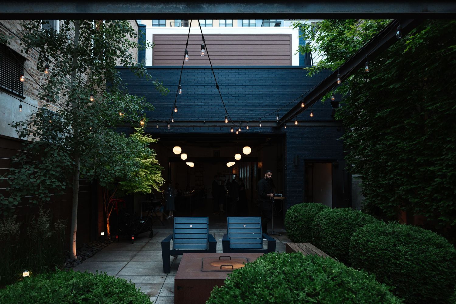 Elegant outdoor courtyard venue at dusk with string lights and manicured hedges.
