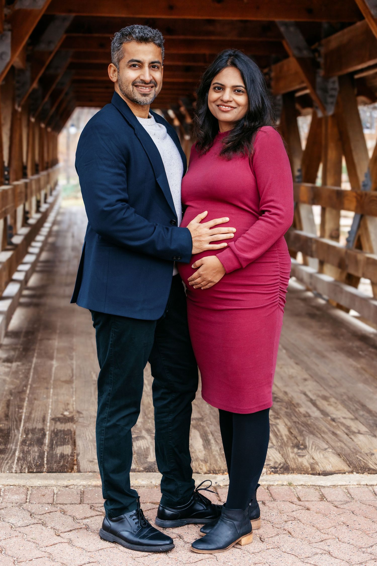 Couple posing together on wooden covered bridge during outdoor maternity photoshoot.