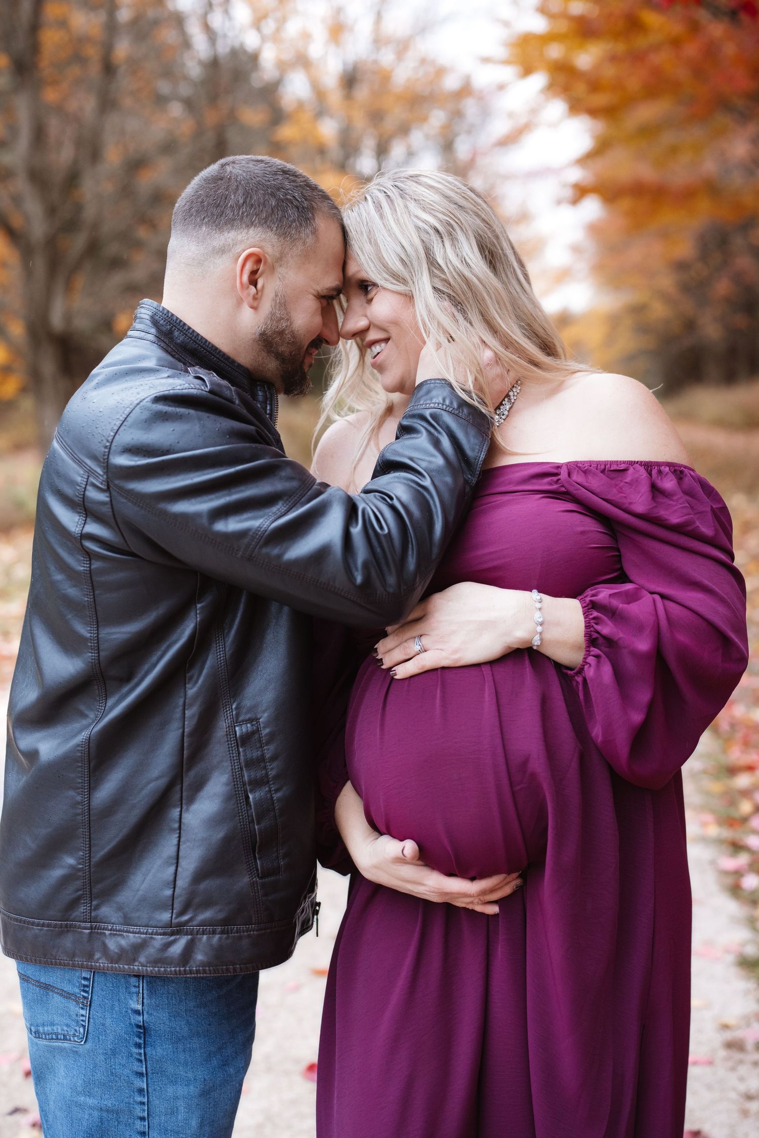 Tender moment between expecting couple touching foreheads during autumn maternity photo session.