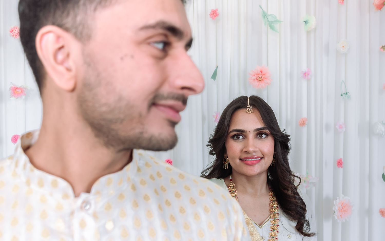 Indian couple sharing a romantic glance during traditional wedding ceremony with floral decorated background.