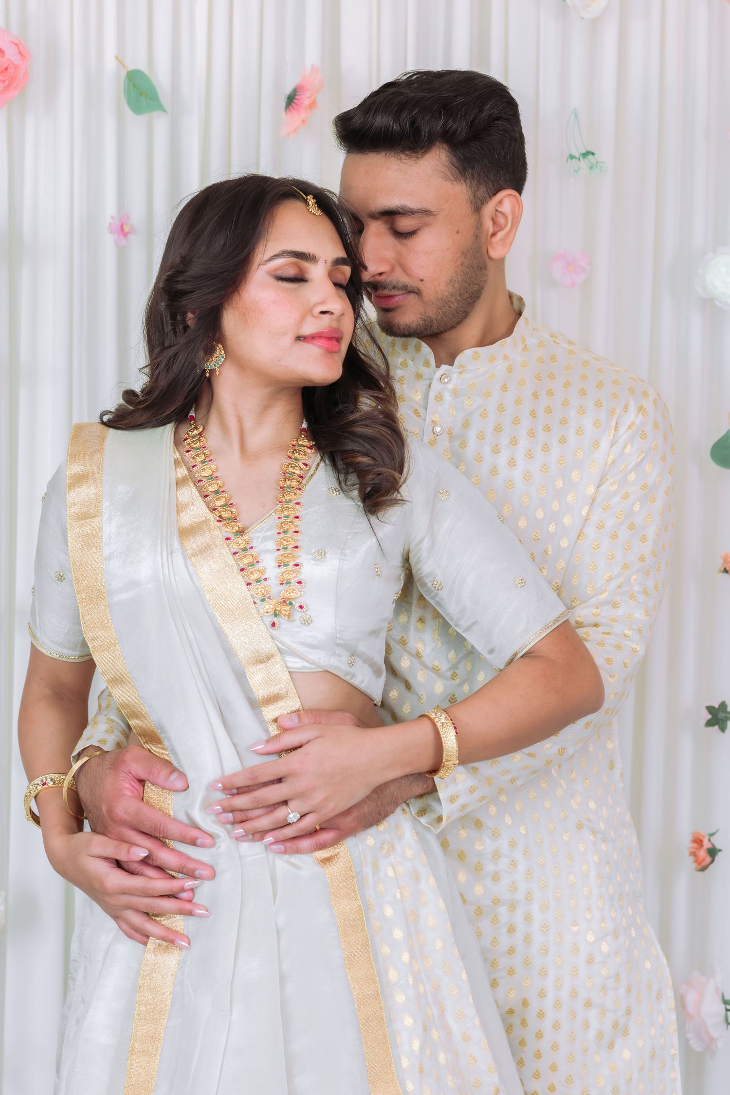 South Asian groom tenderly embracing bride from behind during traditional Indian wedding photoshoot.