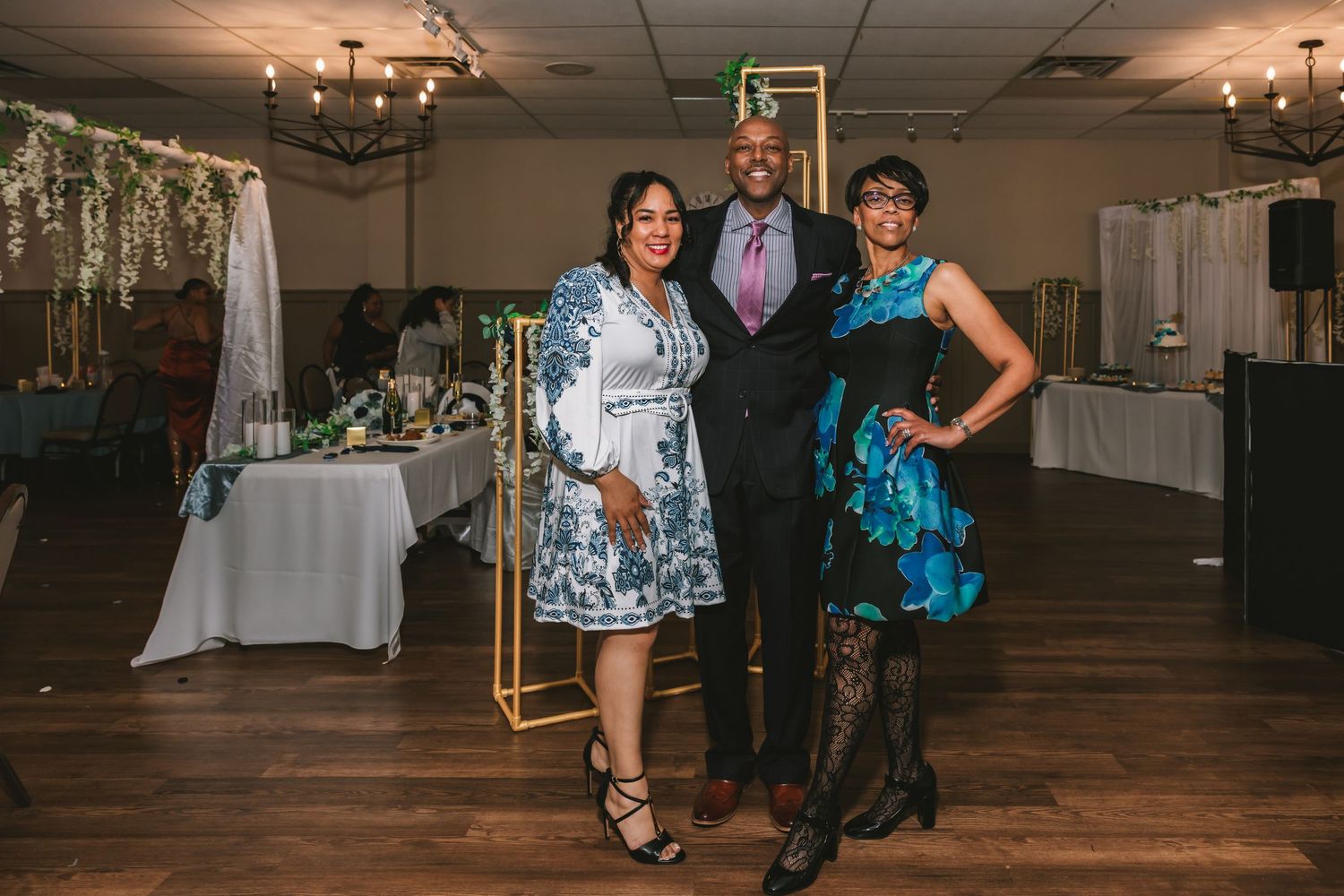 Three guests posing together at an elegant wedding reception venue with gold geometric decor.
