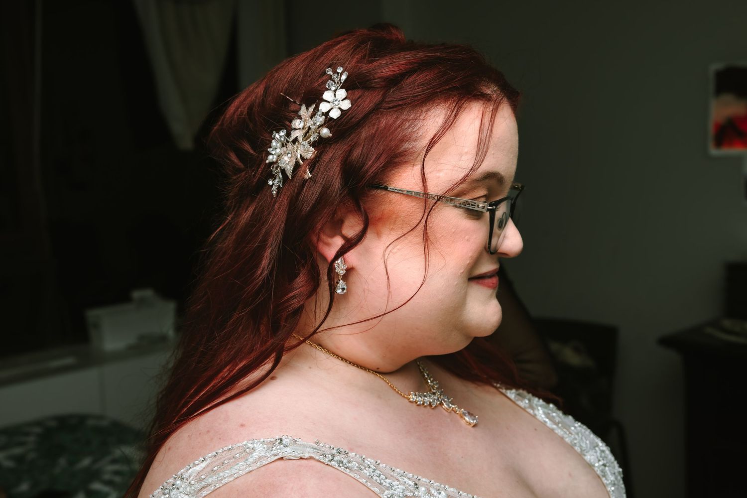 Bride with red hair wearing a floral hair accessory and beaded wedding dress, viewed from the side.
