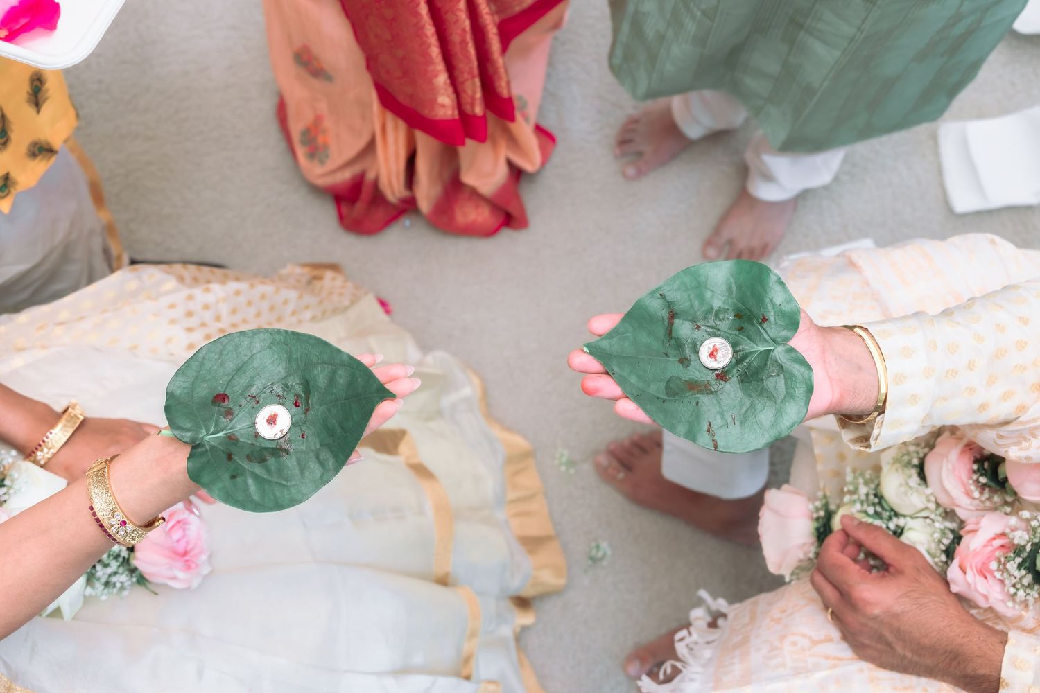 Aerial view of bride and groom holding green betel leaves with silver coins during Hindu wedding ritual.