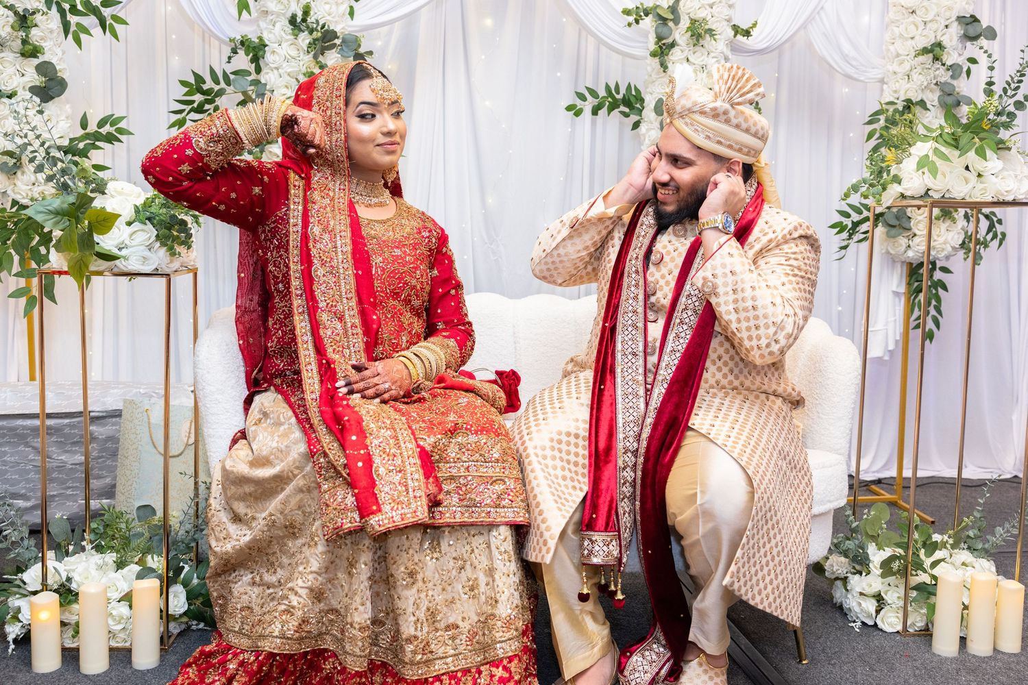 South Asian bride and groom in traditional red and gold wedding attire seated together during ceremony.